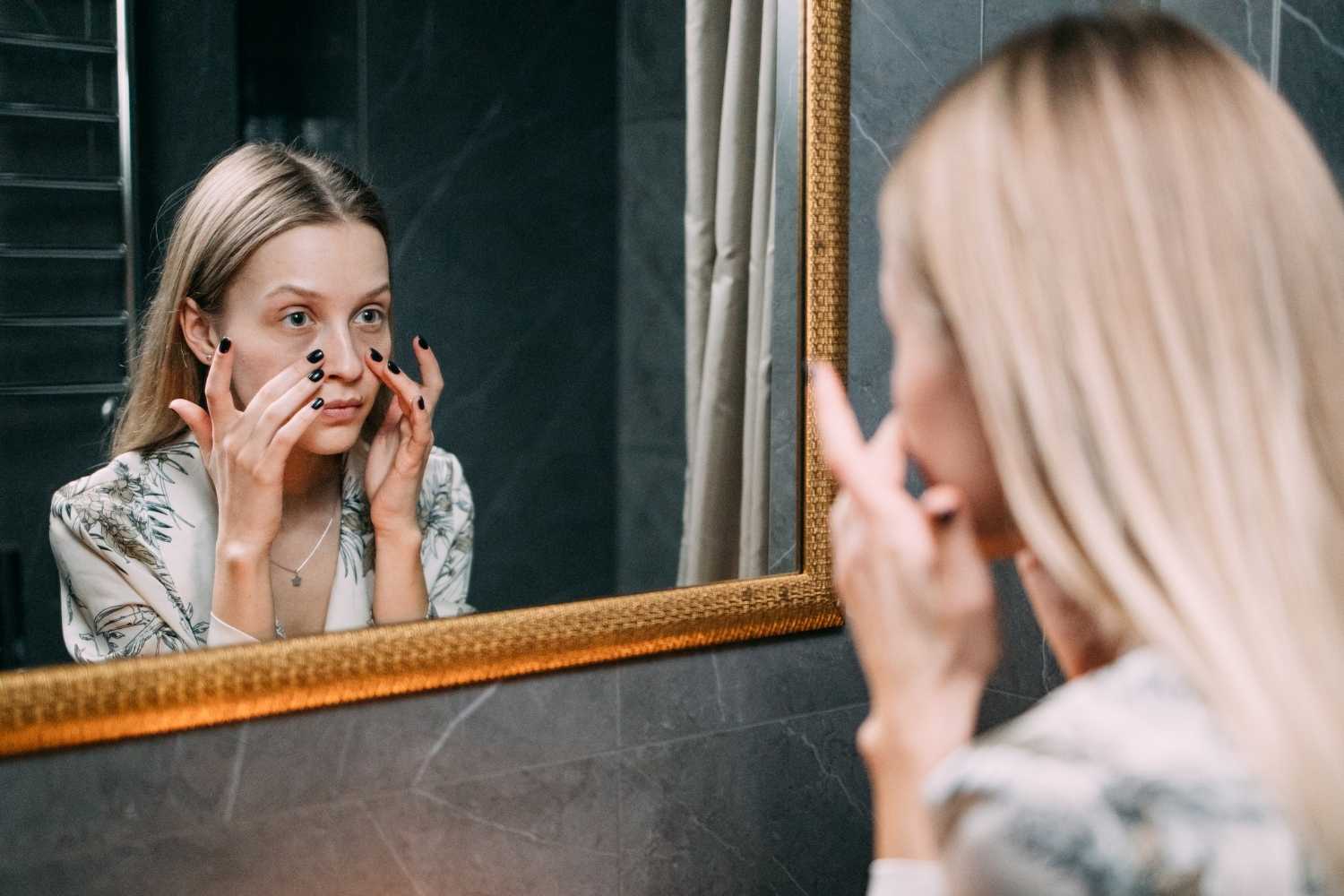 Kvinne i førtiårene som ser seg i speilet, litt bekymret.