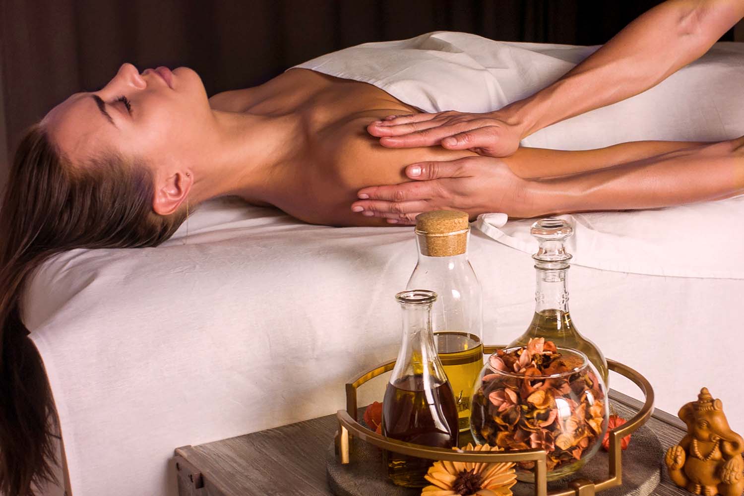 En kvinne som ligger og får ayurvedisk massasje og vi ser noen flasker med oljer i forkant av bildet